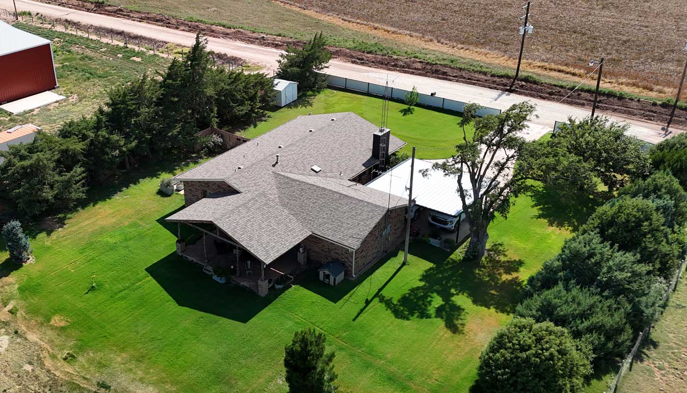 Aerial view of a completed grey shingle roof on a brick house with a green lawn